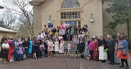 A large group of mostly women gather in front of a building