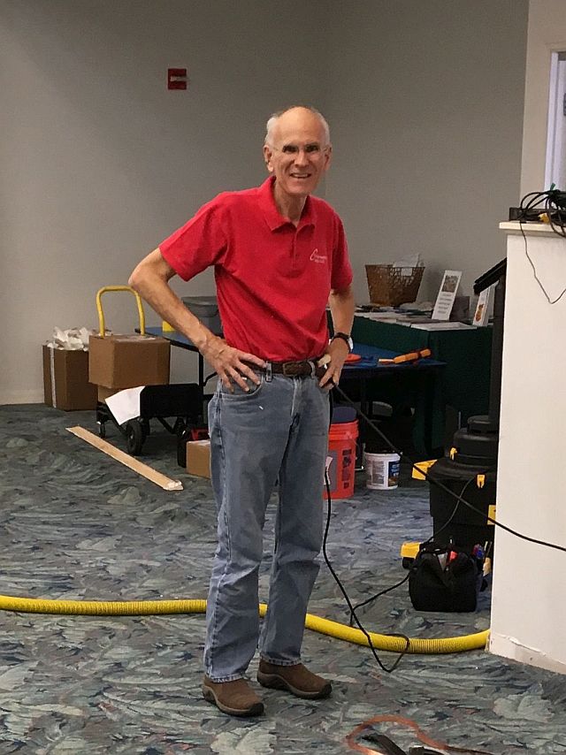 the man in the red shirt is standing in front of some toolboxes, looking at the work.