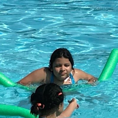 two young women in a pool, swimming with pool noodles.