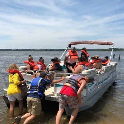 several people ride a pontoon boat as others push it into deeper water