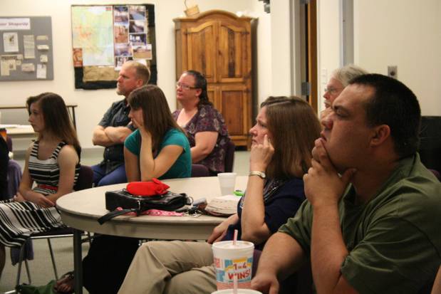 A class with several people sit around tables, watching a speaker who is out of the picture