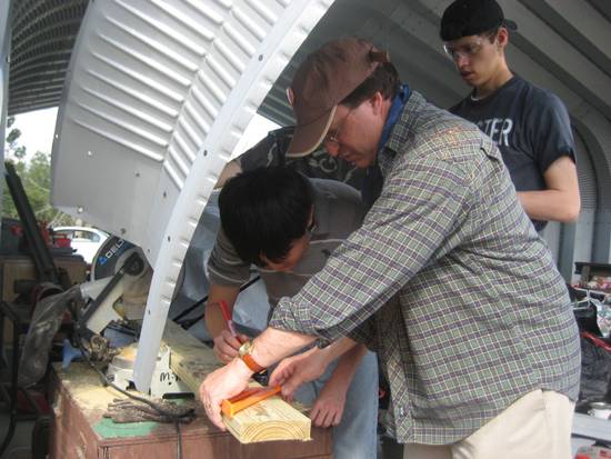 Tom Hudspeth cuts a  piece of wood while others look on